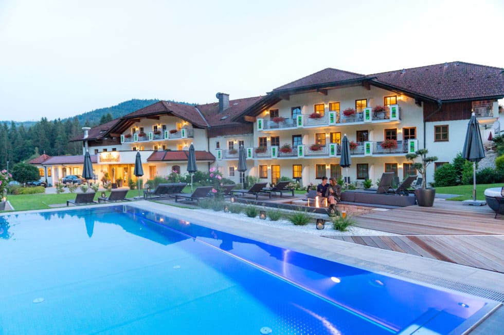 Hotel Hammerhof in Abenddämmerung von außen mit leuchtenden Fenstern und Pärchen vor dem Pool