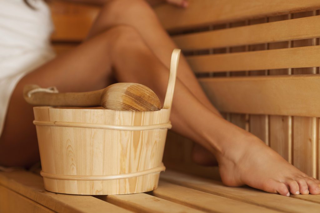 Bein einer Frau in der Sauna mit Holzeimer und Schöpfkelle