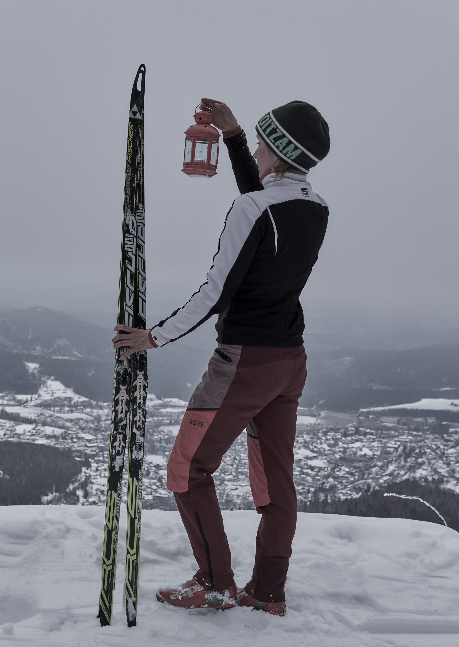 Frau mit Laterne in der Hand steht mit Ski am Gipfel